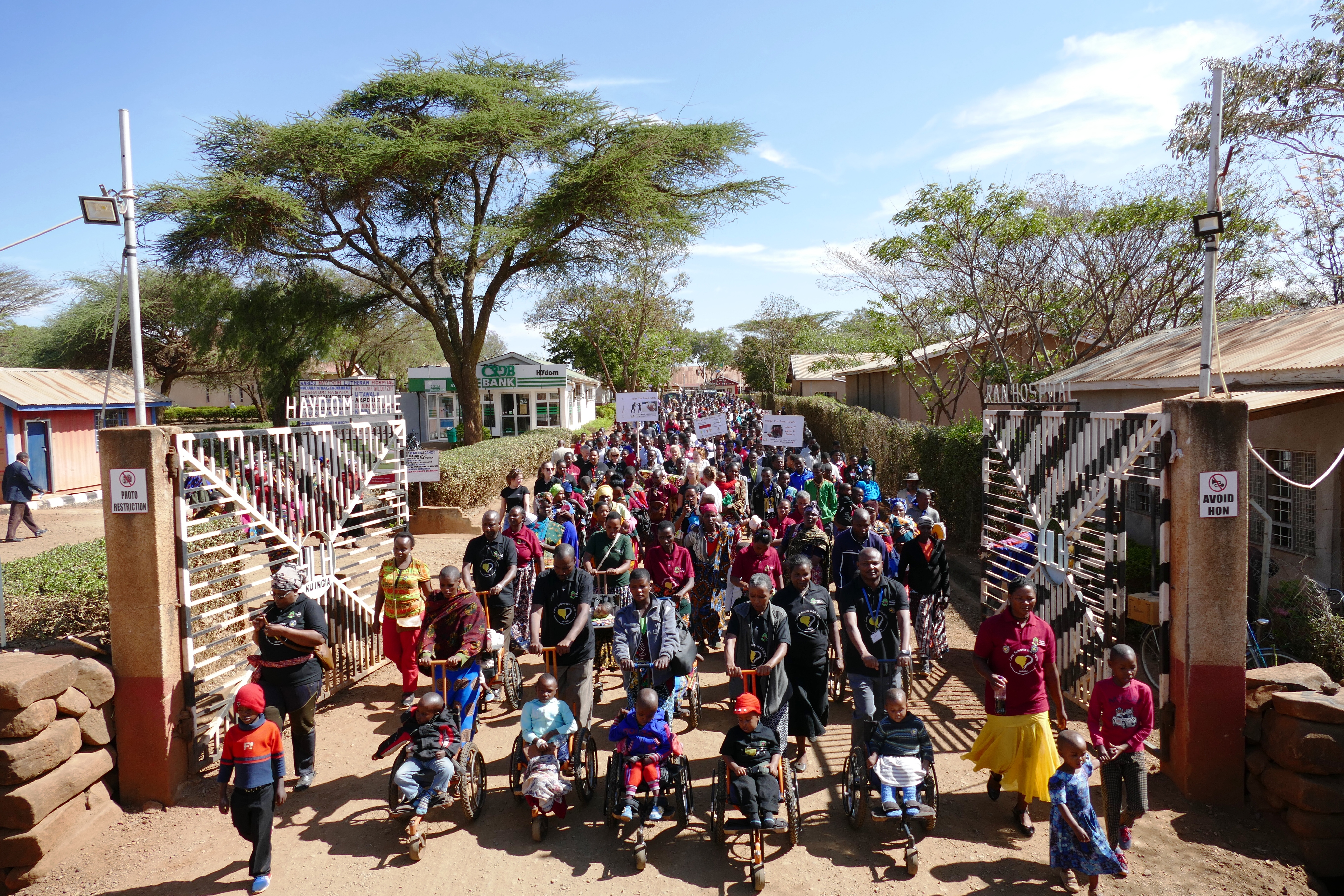 Auf dem Bild verlässt eine große Menschenmenge die Tore der Klinik in Haydom, ganz vorne Kinder im Rollstuhl.