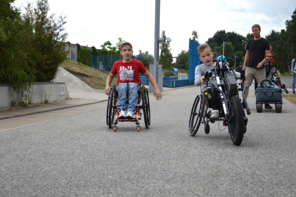 Zwei jungendliche Rollstuhlfahrer - einer in einem Skaterollstuhl, der andere mit einem Handbike