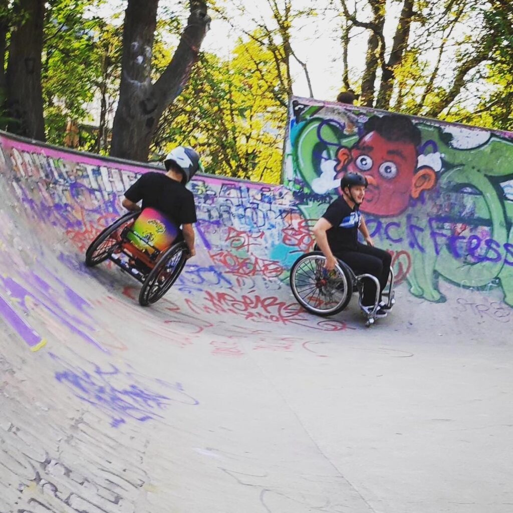 Ein Junge und ein Mann skaten mit Rollstühlen in einem Skatepark