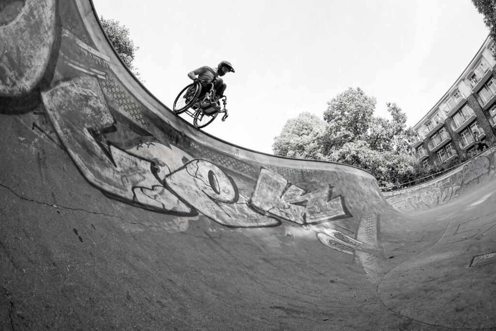 Schwarz/weiß-Bild von David, einem Rollstuhlfahrer, der von oben in eine Skate Bowl hinein fährt