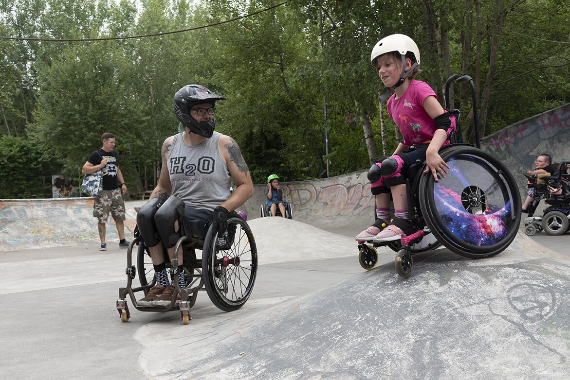 Ein Mädchen und ein Mann, beide im Rollstuhl, in einem Skatepark