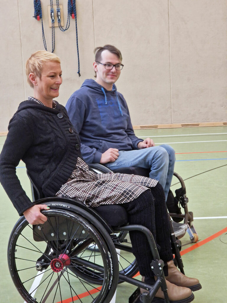 Bezirksamtsleiterin Stefanie von Berg sitzt im Rollstuhl neben David Lebuser, ebenfalls im Rollstuhl.