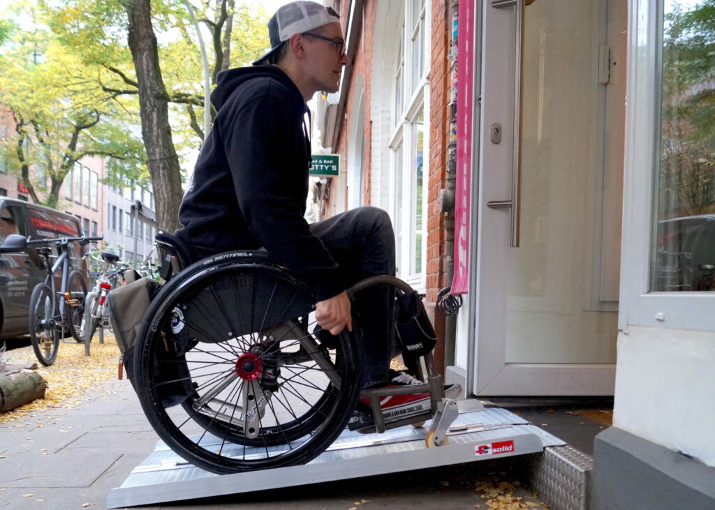 Ein Rollstuhlfahrer fährt auf einer Rampe in ein Geschäft.