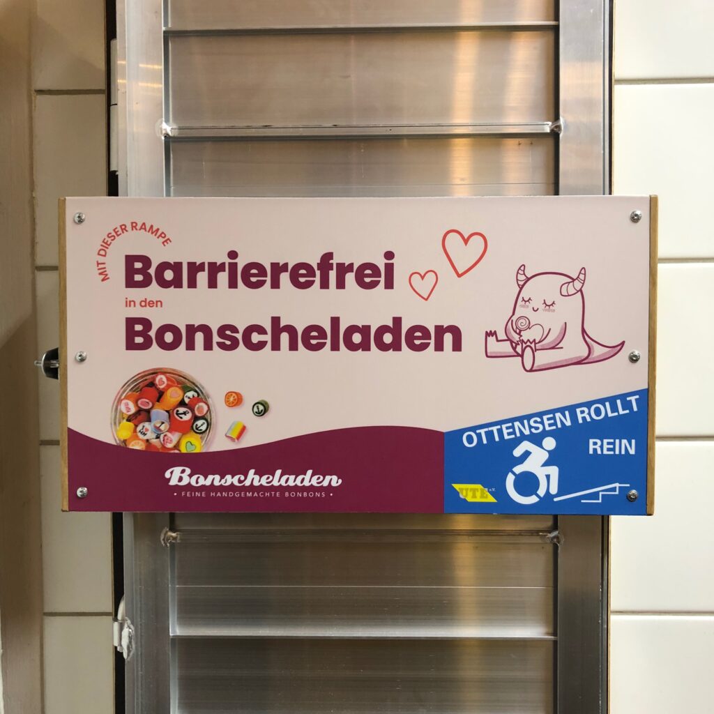 Rampe im Halter mit einem bunten Schild vorne dran: Barrierefrei Bonscheladen. 