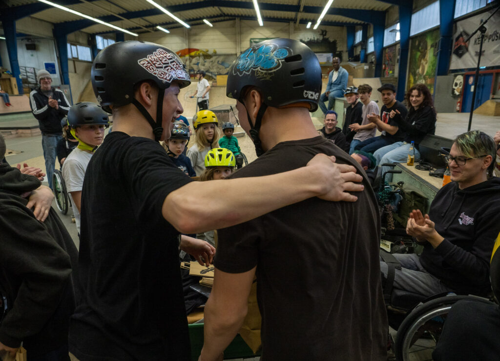  Zwei Jungs umarmen sich mit Freude, drum herum eine Gruppe von Menschen, einige applaudieren.