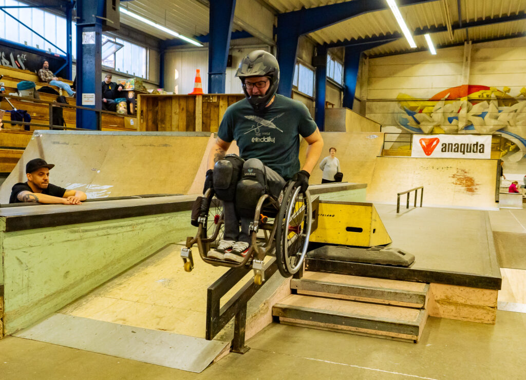 Ein Rollstuhlfahrer grindet in einer Skatehalle auf einem Geländer runter.