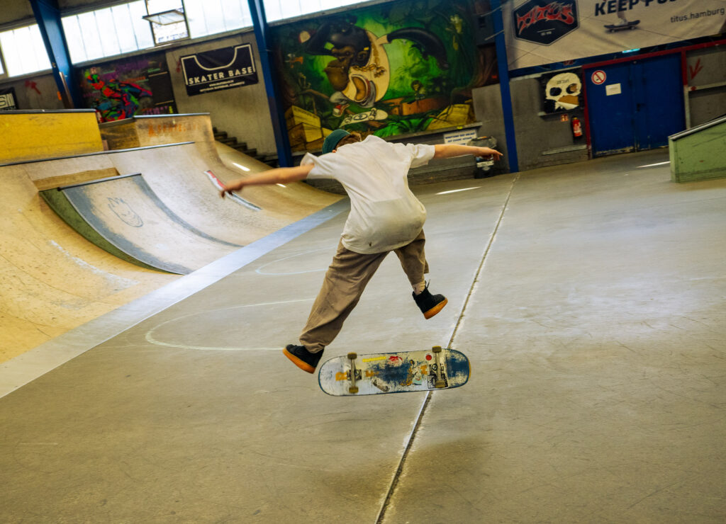 Ein Junge macht in einer Skatehalle mit dem Skateboard einen Kickflip