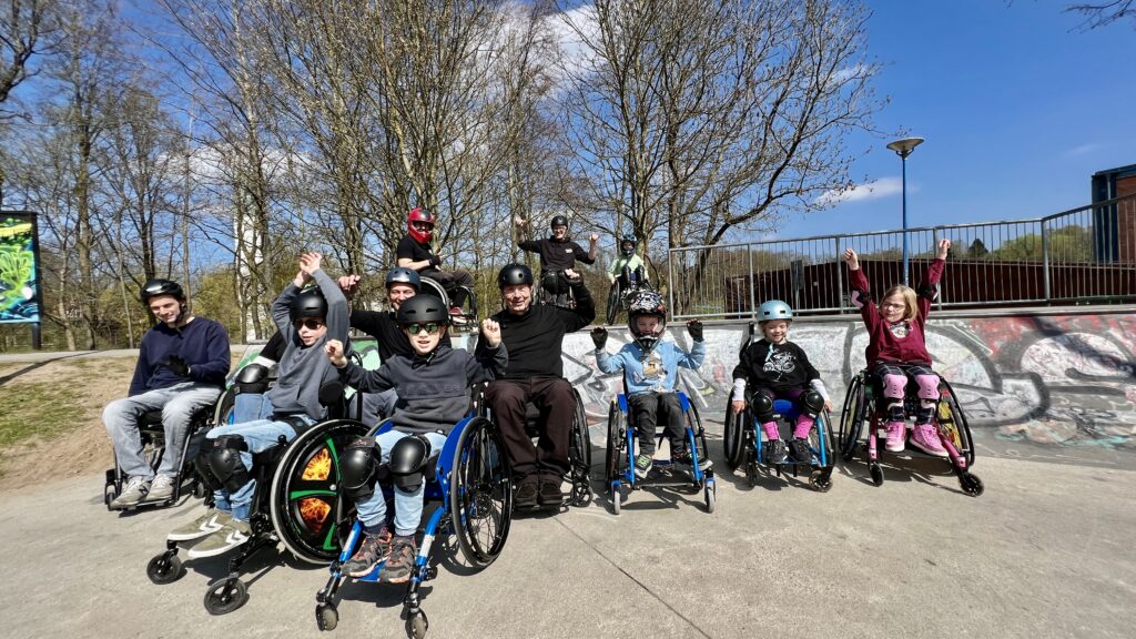 Eine Gruppe von Rollstuhlfahrern und Rollstuhlfahrerinnen im Skatepark