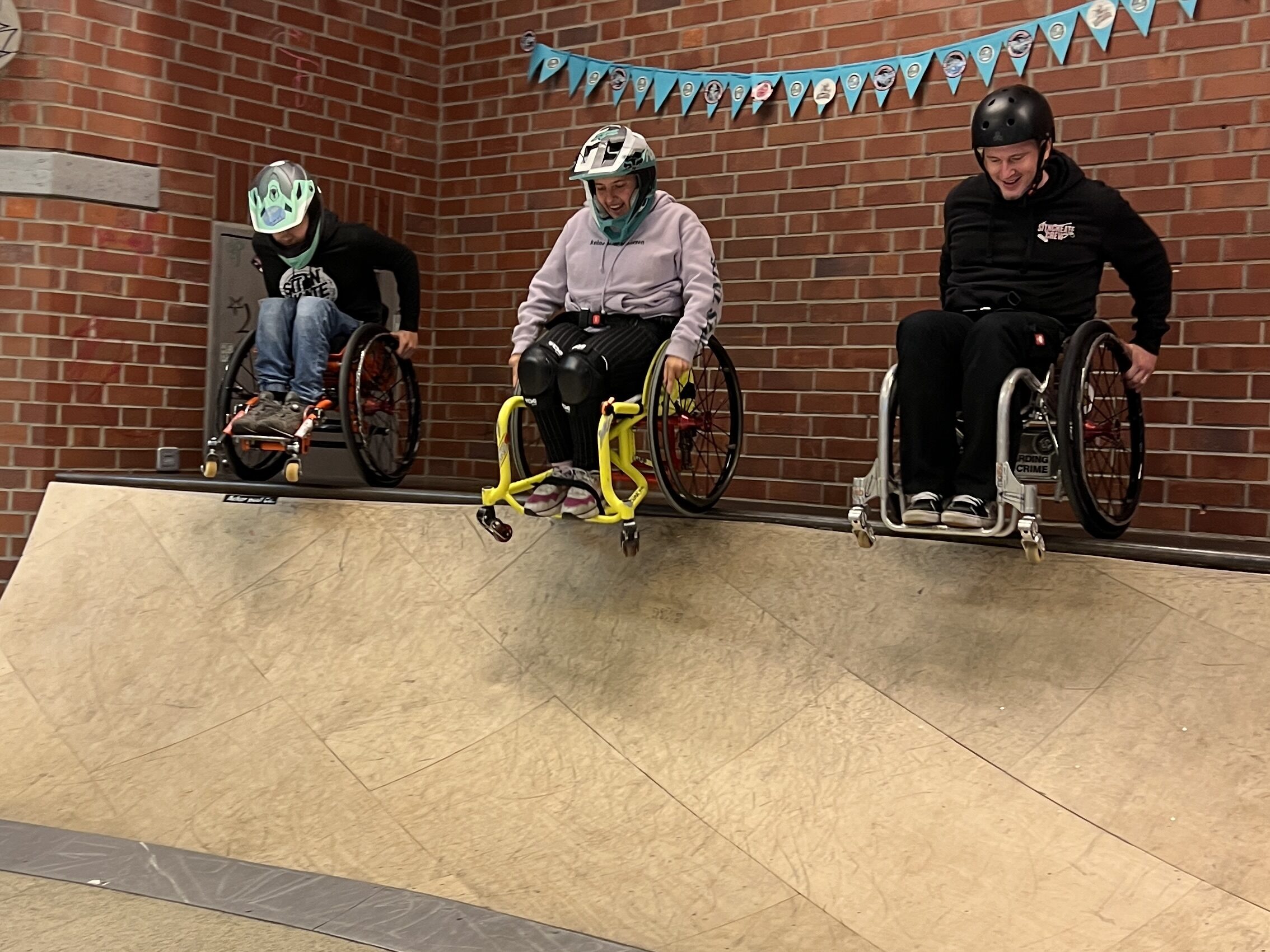 Drei Menschen im  Rollstuhl droppen von einer Quarterramp.