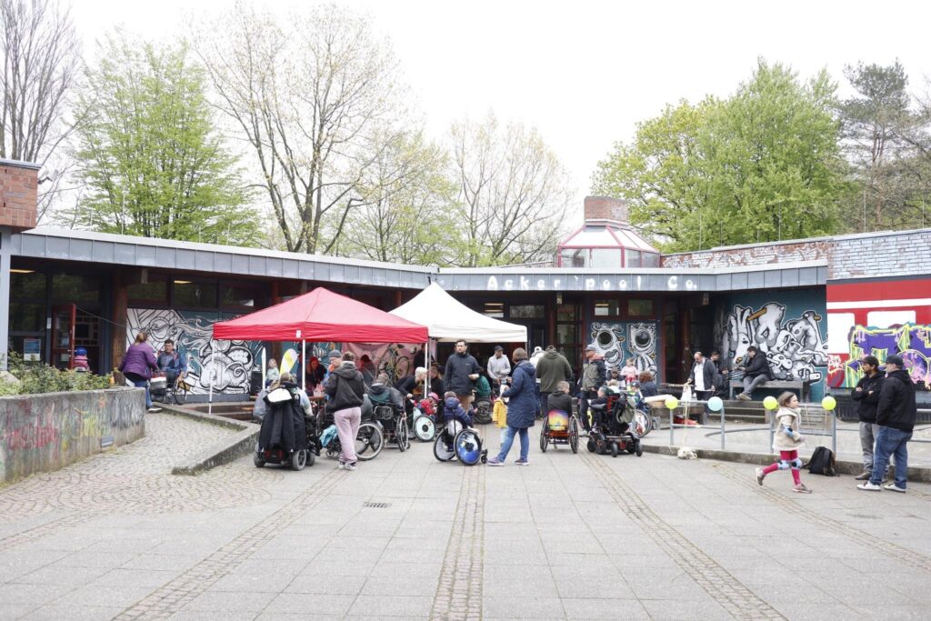 Vor einem Jugendclub sind zwei Pavillons aufgebaut. Es tummeln sich Menschen mit und ohne Rollstuhl davor.