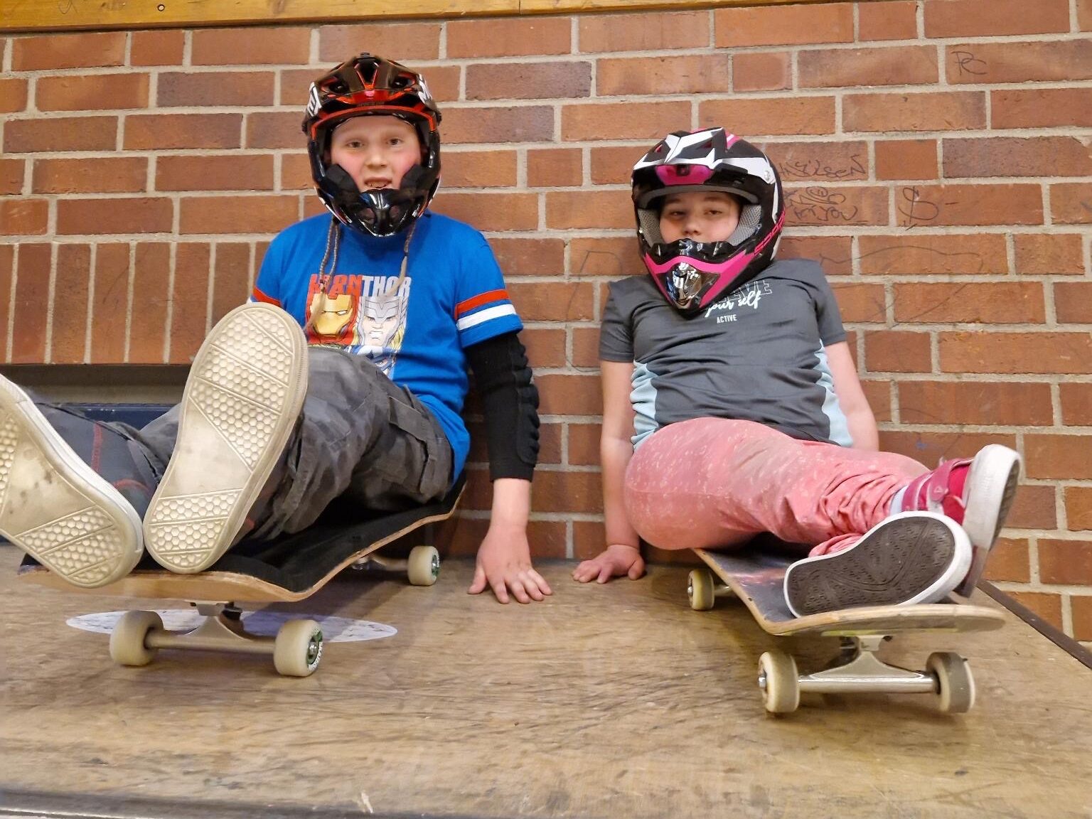 Zwei Kinder sitzen auf Skateboards.