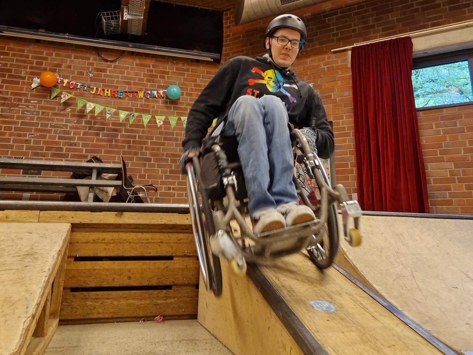 Ein Rollstuhlskater versucht einen Trick an einer Holz Ledge.