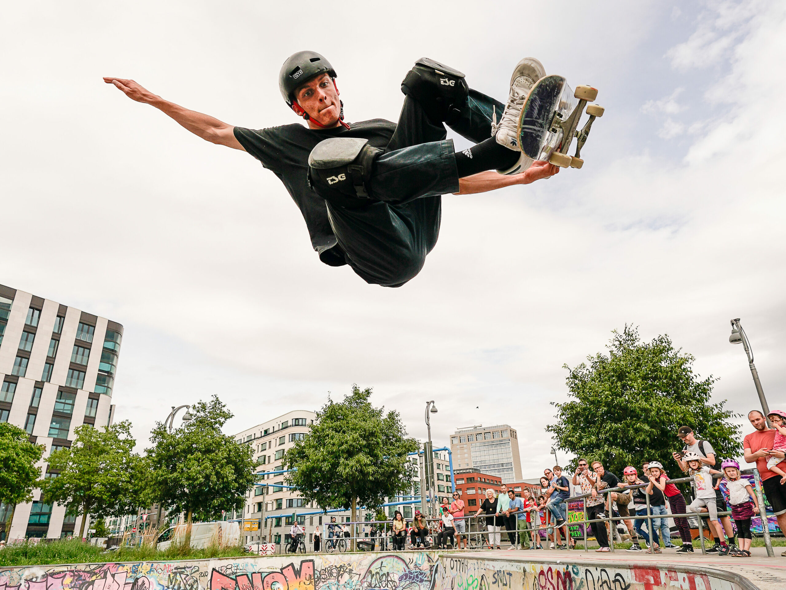 Ein Skateboarder springt sehr hoch aus einer Bowl und hält das Skateboard unter ihm fest während er in der luft schwebt.