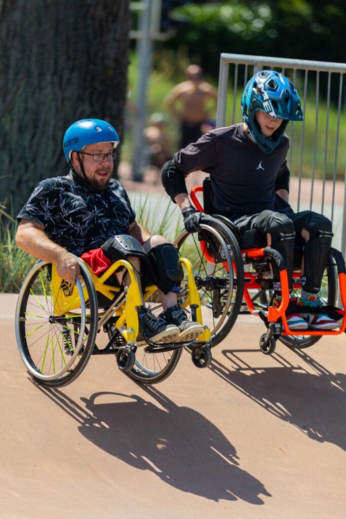 Zwei Rollstuhlfahrer fahren in eine Rampe im Skatepark.