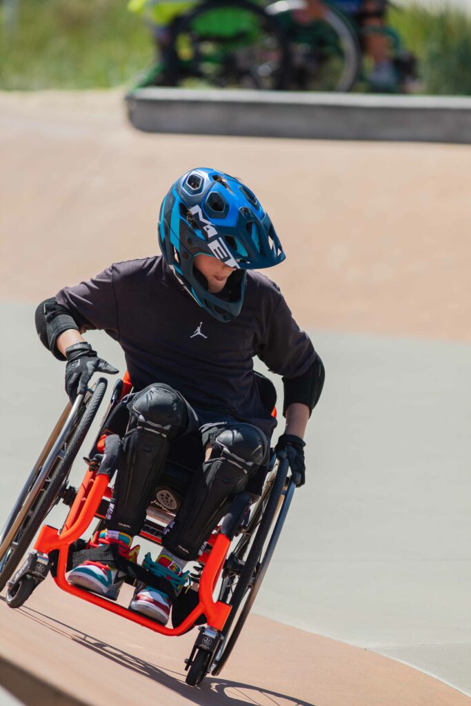 Ein Rollstuhlfahrer fährt an einer schrägen Rampe im Skatepark.