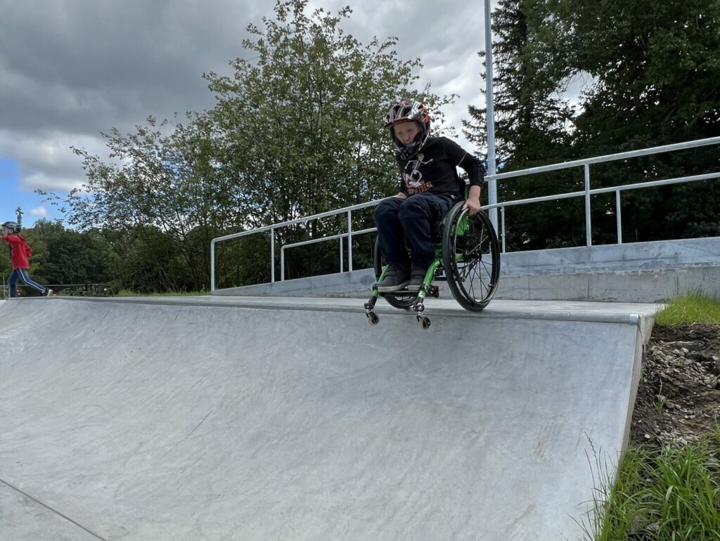 Ein Junge im Rollstuhl droppt von einer Rampe im Skatepark.