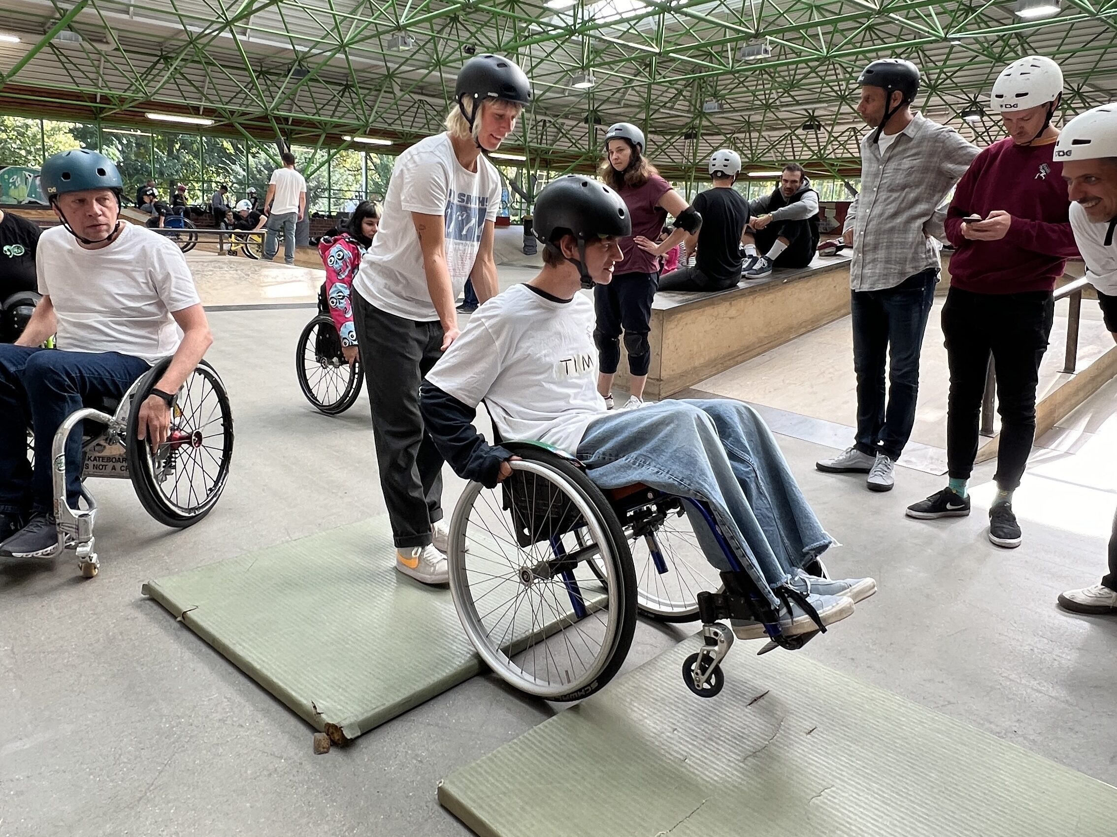 Eine Frau hilft einem Mann im Rollstuhl beim üben auf den Hinterrädern zu stehen.