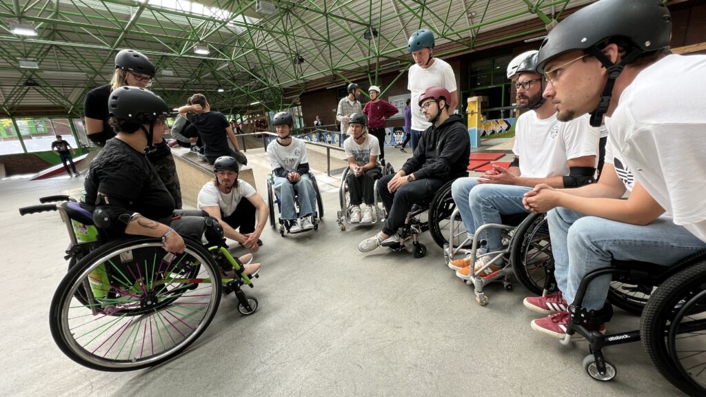 Menschen im Rollstuhl sitzen in einer Skatehalle in einer Runde