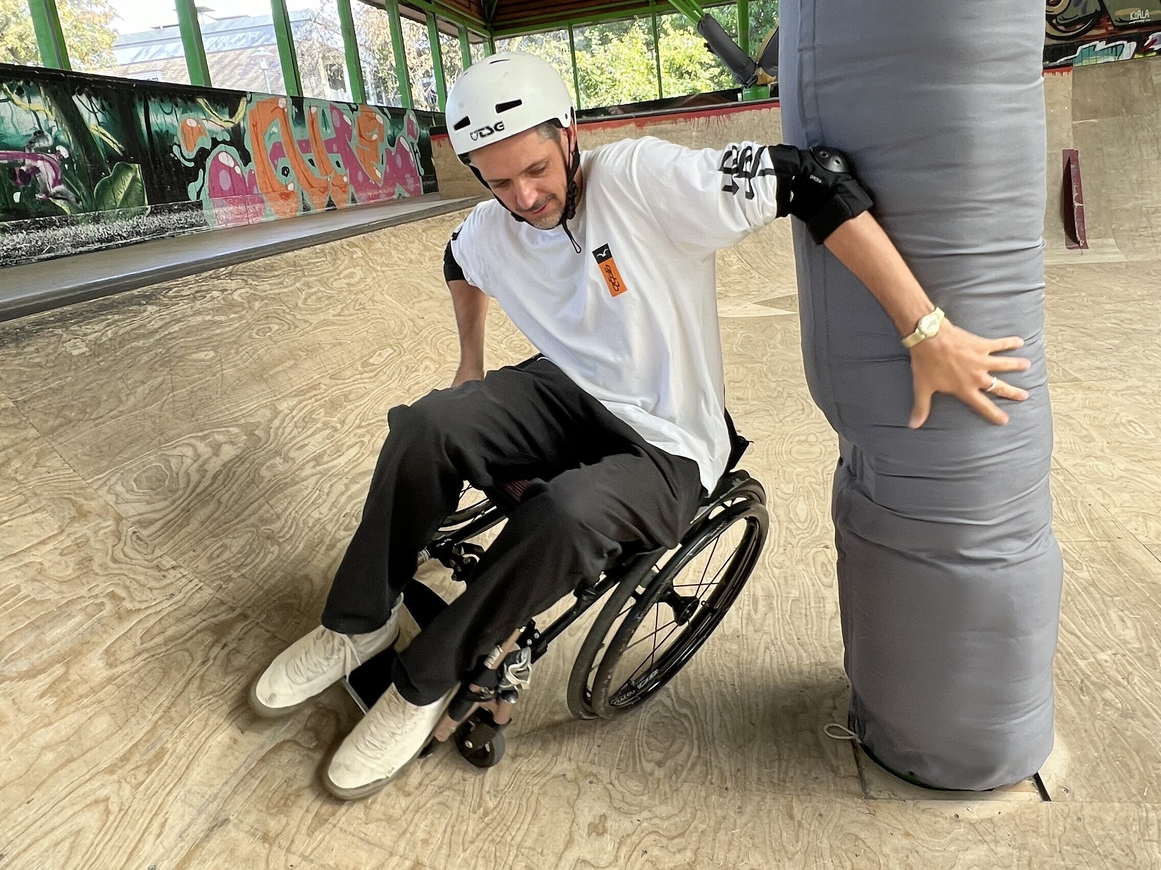 Ein Mann im Rollstuhl versucht um eine Säule zu fahren und stützt sich an der Säule ab.