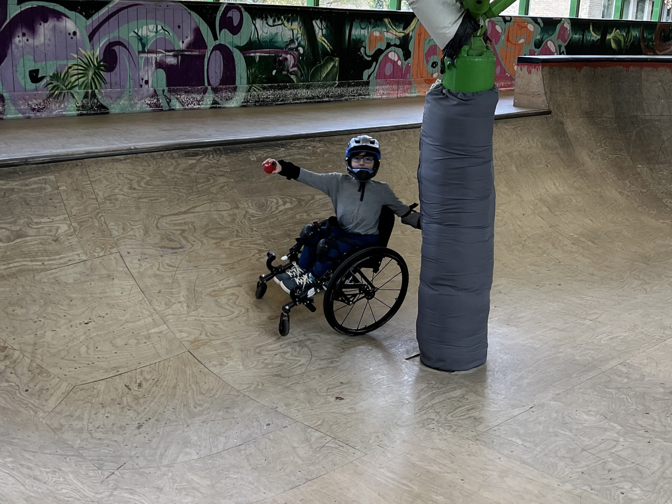 Junge im Rollstuhl fährt in einer Skatehalle um eine Säule.