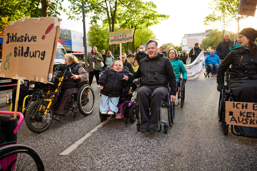 Menschen mit Rollstühlen fahren vorneweg, gefolgt von vielen Demonstrierenden.