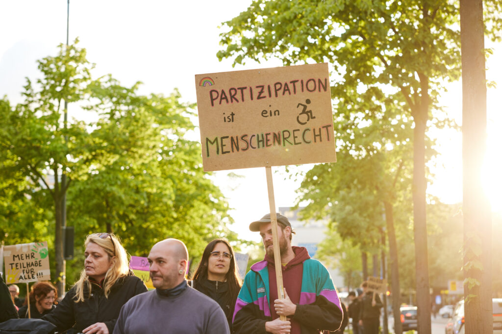 Menschen auf der Reeperbahn im Abendlicht mit Protestschild Partizipation ist ein Menschenrecht.