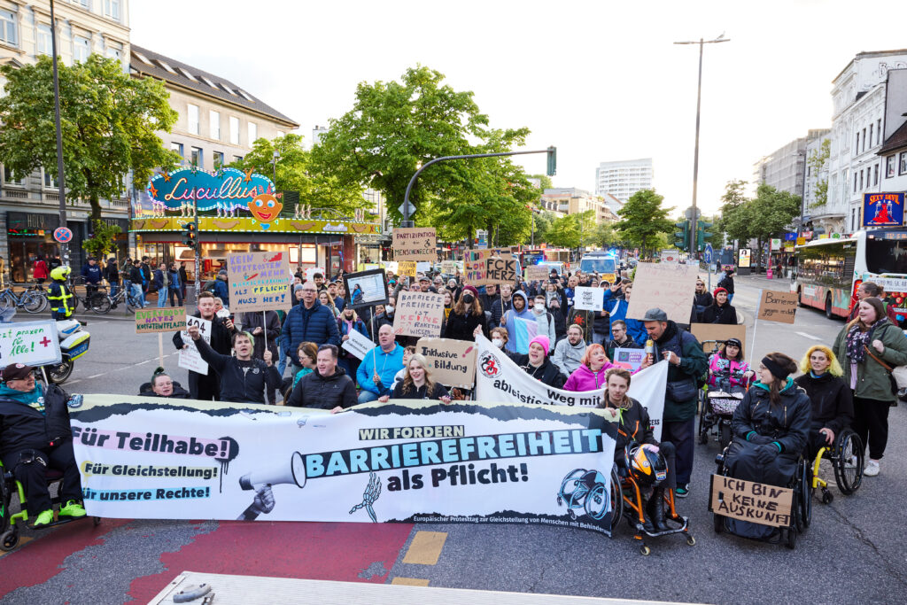 Transparent „Barrierefreiheit als Pflicht“ vor der demonstrierenden Gruppe.