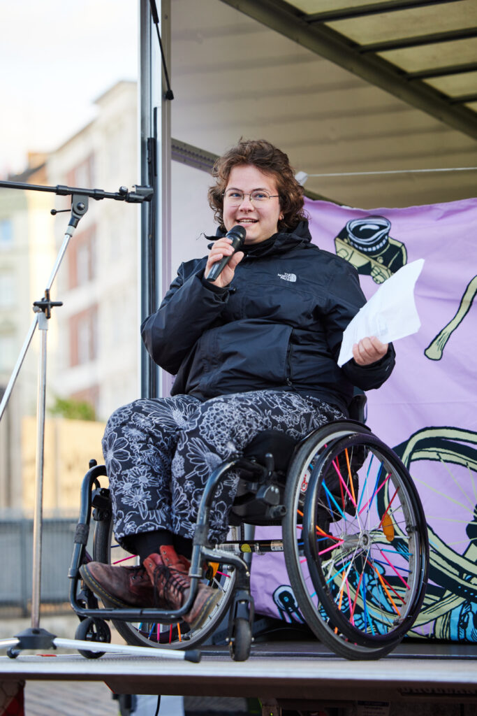 Person im Rollstuhl spricht auf der Bühne vor Publikum.