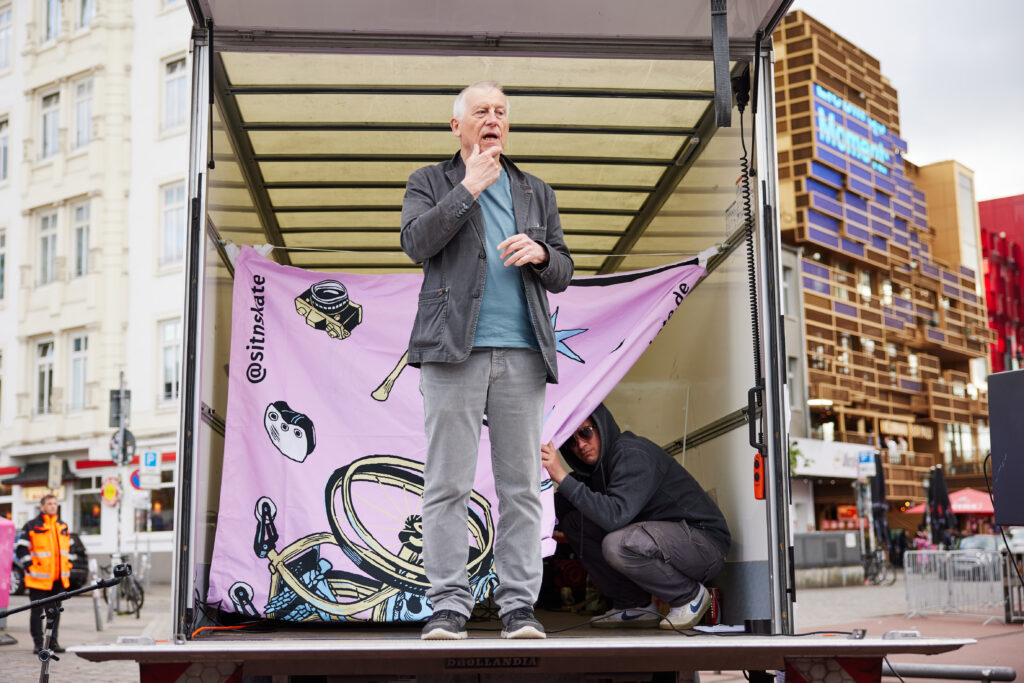 Eine Person auf der Bühne macht Gebärdensprache, Zuschauer*innen hören zu.