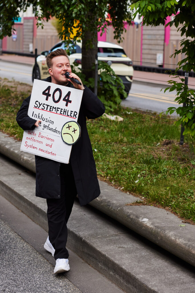 Person mit Mikrofon und einem Schild „404 Inklusion nicht gefunden“.