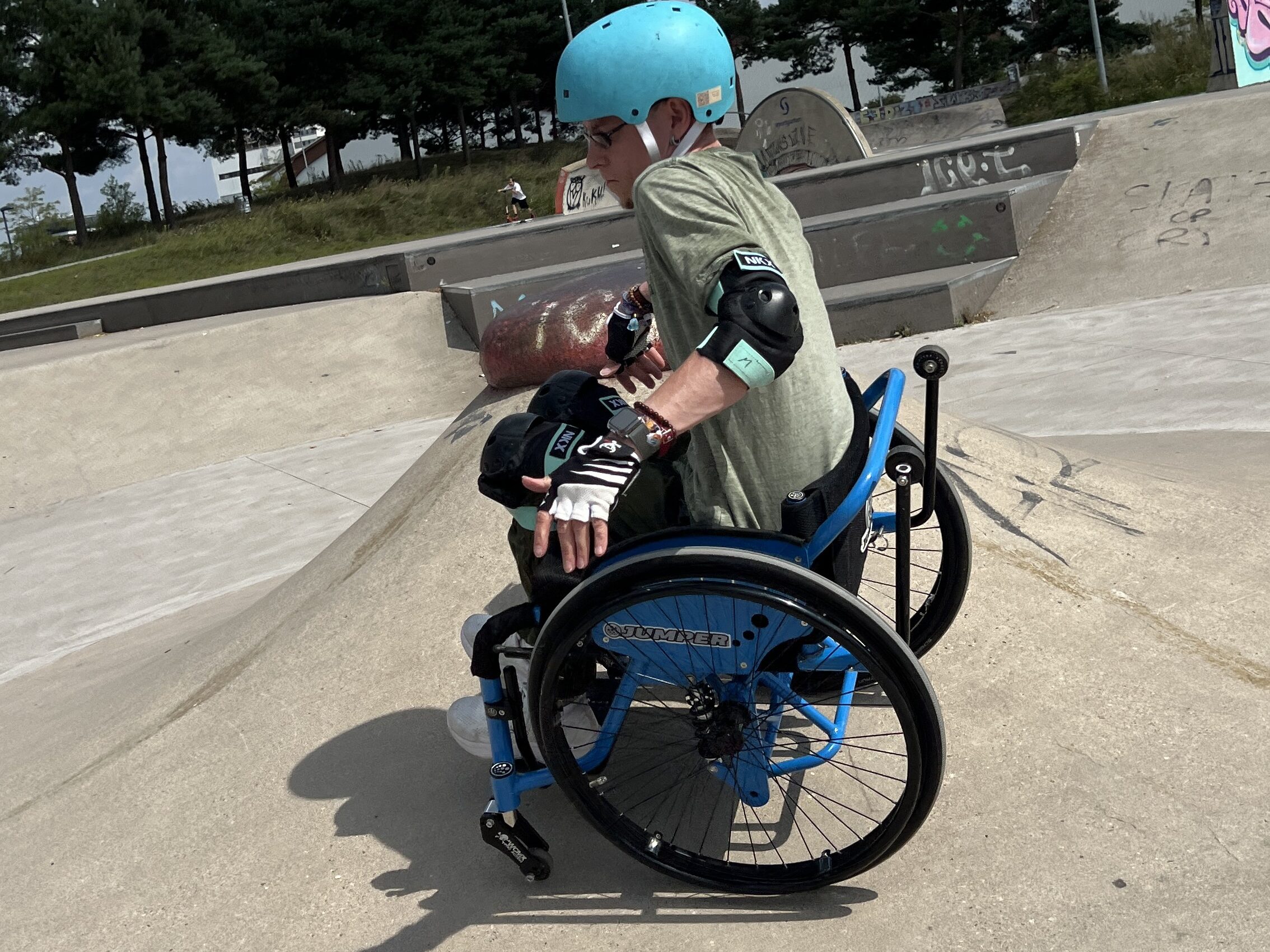 Ein Mann im Rollstuhl fährt im Skatepark seitlich an einem Vulkanförmigen Element entlang.