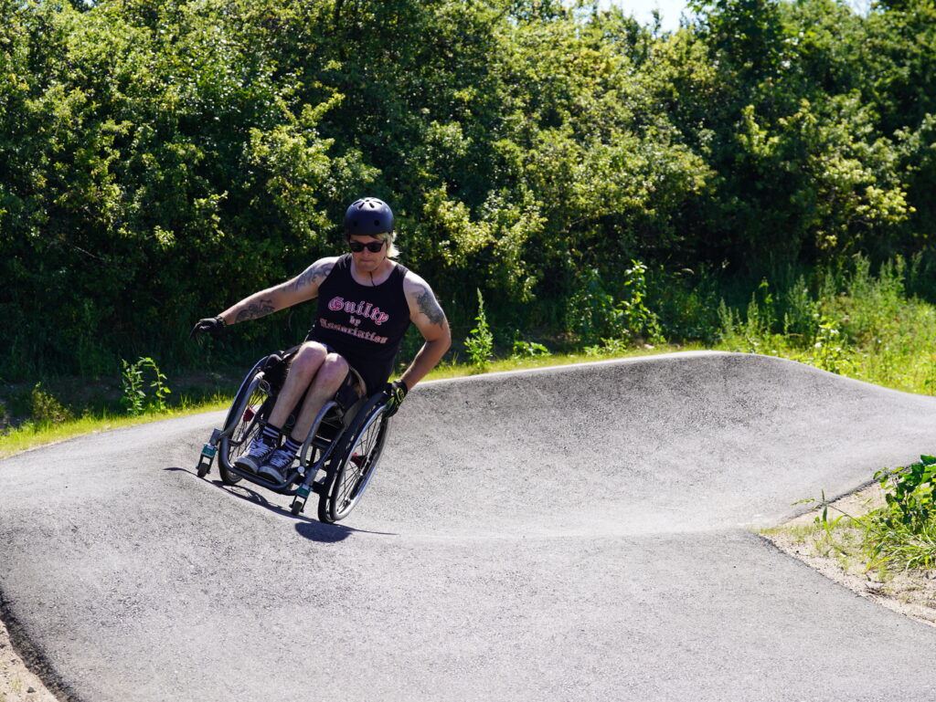 Ein Rollstuhlfahrer auf einem asphaltierten Pumptrack am Ausgang einer Kurve.