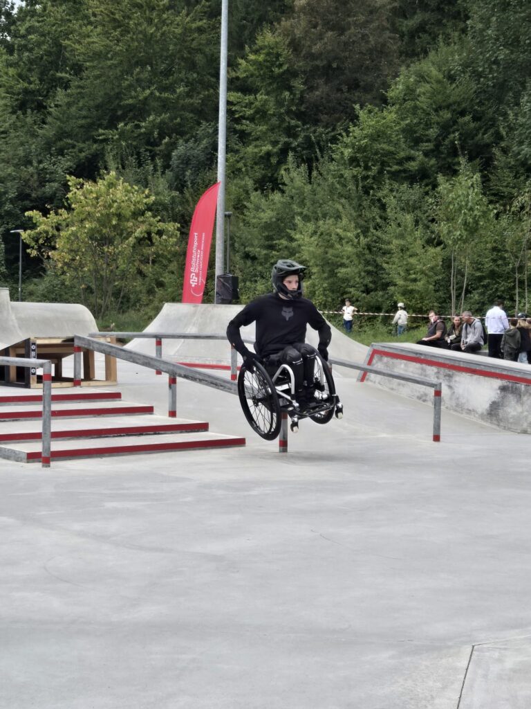 Ein Rollstuhlfahrer im Skatepark auf einem langen Downrail grinded.
