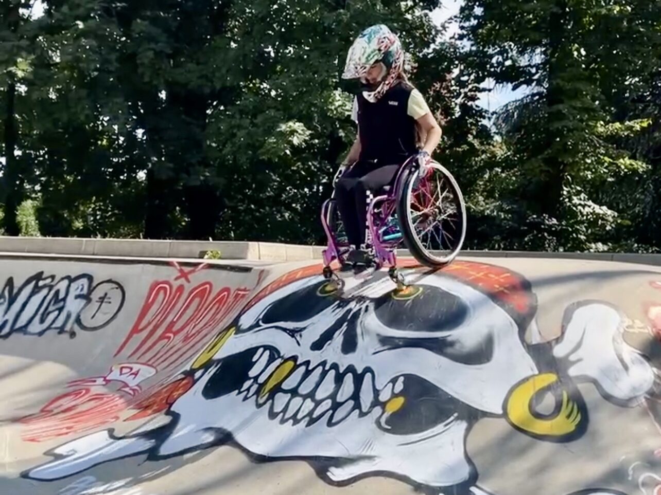 Ilaria mit ihrem lila Rollstuhl beim einfahren in einen Roll In im Skatepark mit einem Piraten Skull Graffiti.