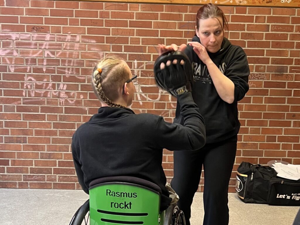 Ein Jugendlicher Rollstuhlfahrer im Übungskampf mit der Trainerin.