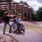 Eine Frau schiebt ein Kind im Rollstuhl über den Pumptrack
