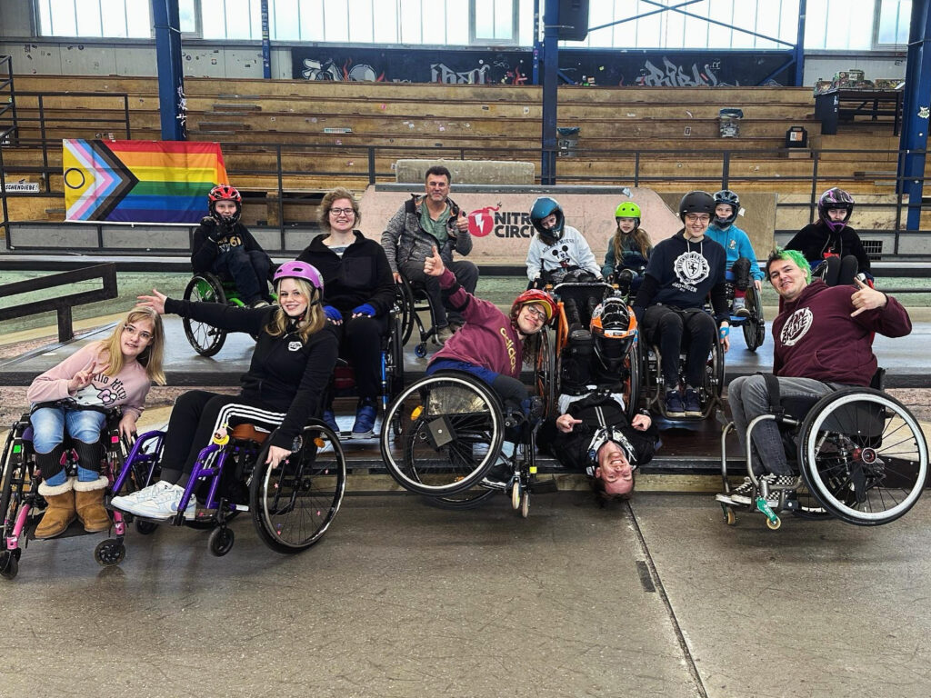 Gruppenbild von Menschen im Rollstuhl in einer Skatehalle. 