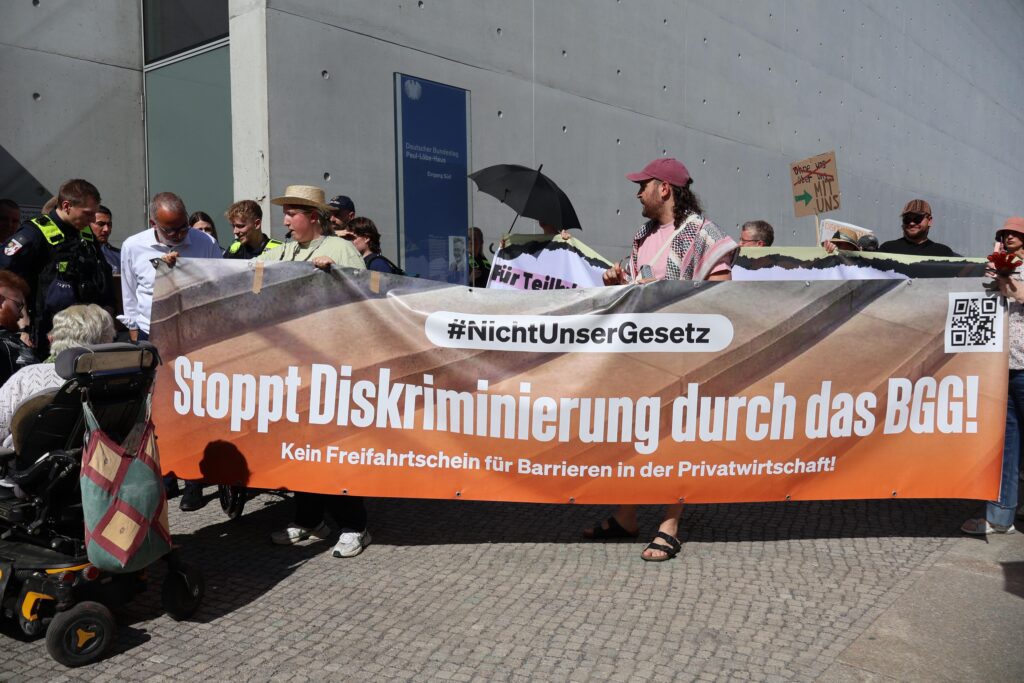 Demonstrierende vor dem Paul-Löbe-Haus halten ein großes Banner mit der Aufschrift „#NichtUnserGesetz – Stoppt Diskriminierung durch das BGG! Kein Freifahrtschein für Barrieren in der Privatwirtschaft!“.