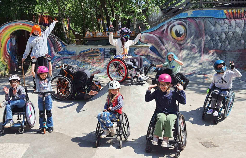 Gruppenbild von Menschen mit und ohne Rollstuhl in einem bunten Betonskatepark.