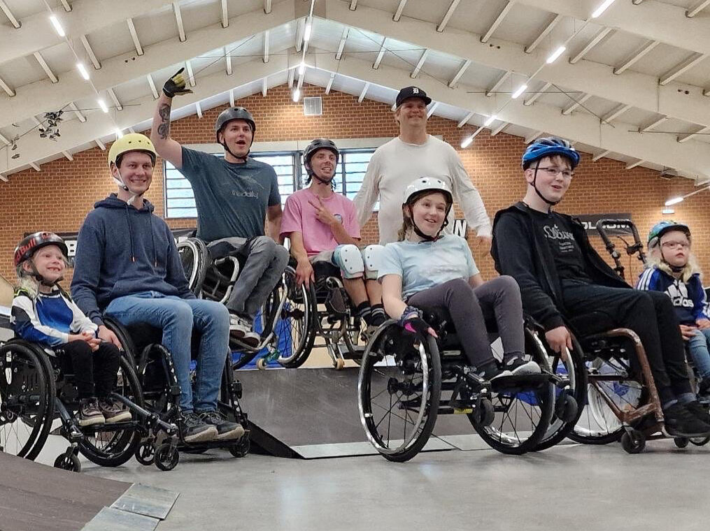 Foto von Menschen mit und ohne Rollstuhl in einer Skatehalle.