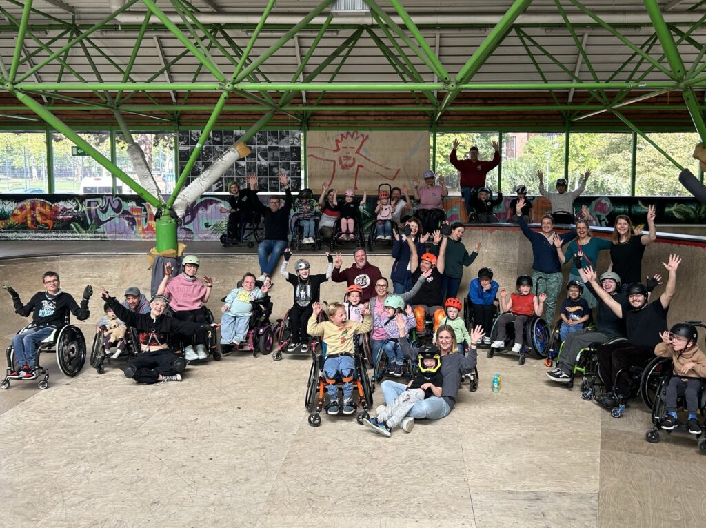 Gruppenbild von vielen Menschen mit und ohne Rollstuhl in einer Skatehalle
