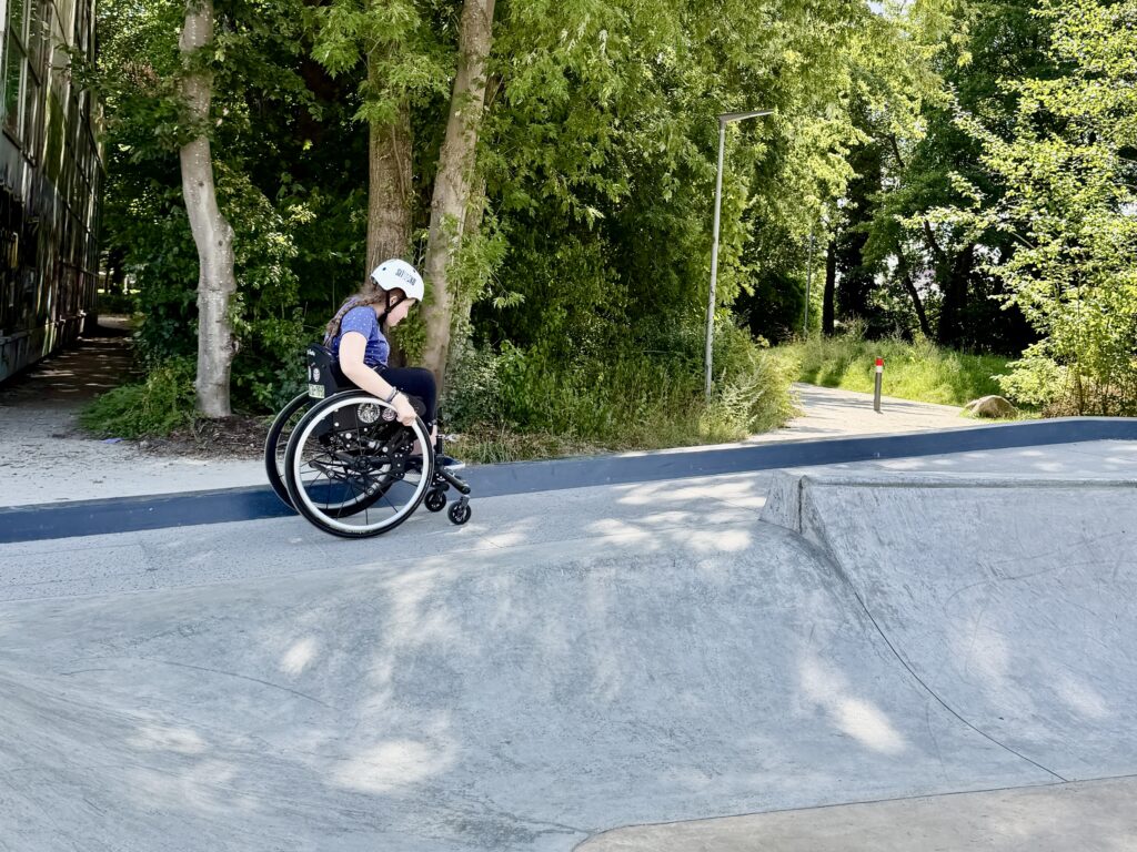Eine Jugendliche Rollstuhfahrerin fährt eine Rampe im Skatepark hoch.