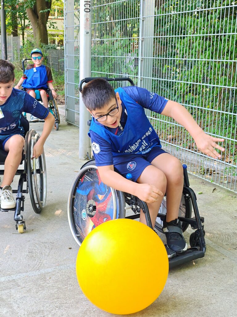 Ein Junge im Rollstuhl spielt einen gelben Gymnastikball.