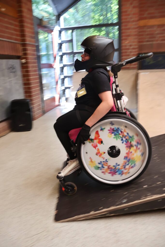 Eine Jugendliche im Rollstuhl mit Helm fährt rasant eine Rampe herunter.