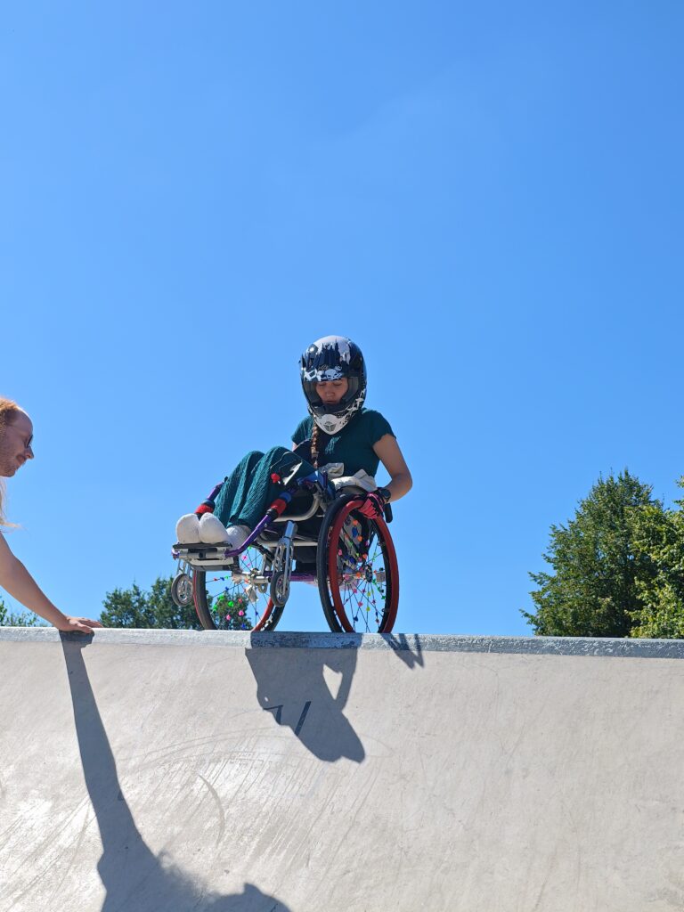 Eine Rollstuhlfahrerin beim Drop In in eine Rampe im Skatepark von unten aufgenommen.